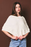 Woman wearing a white knitted poncho against a brown background