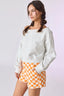 Woman wearing a white sweater and orange checkered shorts on a light gray background