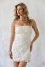 Woman wearing a white lace strapless dress against a plain background