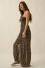 Woman wearing a strapless, long, patterned dress against a beige background