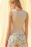 Woman wearing a light-colored sleeveless top and floral pants against a yellow background