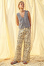 Woman wearing a sleeveless top and patterned pants standing against a light curtain background