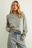 Woman wearing a gray sweater and plaid pants against a plain background