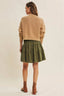 Woman wearing a beige sweater and green skirt on a plain background