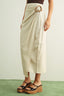 Person wearing a beige wrap skirt with a belt on a plain background