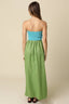 Woman wearing a strapless green dress with a blue top on a beige background