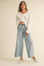 Woman wearing a white blouse with ruffled details and light blue jeans on a beige background
