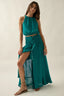 Woman wearing a teal outfit with a long skirt and top on a plain background