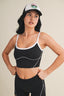 Woman wearing a black sports bra and leggings with a white cap on a beige background