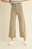 A person wearing high-waisted, wide-leg cropped pants in a light khaki-beige color, paired with a striped top and white sneakers, against a plain beige studio background.