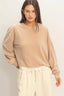 Woman wearing a beige sweatshirt and cream pants against a plain background
