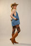 Woman wearing a denim romper, cowboy hat, and brown boots on a plain background
