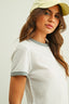 Woman wearing a light gray ribbed sweater and beige cap against a plain background