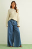 Woman wearing a beige sweater and blue jeans against a plain background