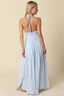 Woman wearing a light blue maxi dress with thin straps on a beige background