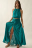 Woman wearing a teal outfit with a halter top and long skirt on a plain background