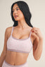 Woman wearing a light pink bralette with thin straps on a plain background
