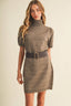 A woman modeling a taupe brown short-sleeve knit turtleneck dress with a matching wide belt featuring a gold buckle, set against a plain beige background.
