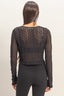 Person wearing a black lace top and black pants on a beige background