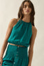 Woman wearing a teal halter top and skirt set against a neutral background