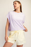 Woman wearing a light purple top and yellow shorts on a plain background