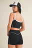 Person wearing a black sports bra and shorts with a cap on a beige background