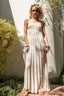 Woman in a long white dress standing outdoors with plants and a wall in the background