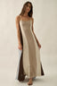 Woman wearing a long, beige dress with a slit on a plain background