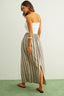 Woman wearing a white strapless top and striped maxi skirt on a plain background
