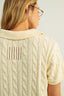 Person wearing a cream-colored cable knit sweater with a plain background