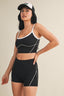 Woman wearing a black athletic outfit with white accents on a beige background