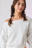 Woman wearing a light gray off-shoulder sweater against a white background