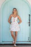 Woman in a white dress with sailboat pattern standing in front of a light blue door.
