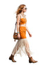 A woman walking at an outdoor festival wearing a bright orange sleeveless crop top and matching fringe skirt, paired with brown ankle boots and a tan shoulder bag.