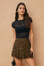 Woman wearing a black lace top and leopard print skirt against a beige background