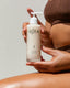 Person holding an OSEA anti-aging body balm bottle against a neutral background