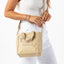 Beige handbag held by a person wearing a white outfit on a white background