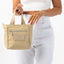 Beige handbag held by a person wearing white pants on a white background