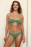 Woman wearing a green bikini with white trim against a beige background