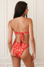 Woman wearing a red floral bikini set against a white paneled wall.