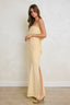 Woman wearing a strapless yellow dress with a slit on a plain background
