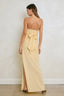 Woman wearing a strapless yellow gown with a bow detail on a plain background