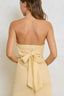Woman wearing a yellow strapless dress with a bow detail on a plain background