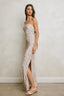 Woman wearing a strapless, patterned gown with a slit standing against a plain wall.