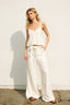 Woman wearing a white sleeveless top and wide-leg pants against a plain background