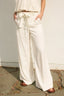 Person wearing a white outfit with wide-leg pants on a stone floor.