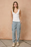 Woman wearing a white tank top and light blue cargo pants against a beige wall.