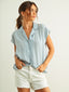 Woman wearing a light blue button-up shirt and white shorts on a plain background