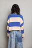 Person wearing a blue and beige striped sweater with a plain background