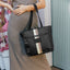 Person holding a black tote bag with a striped design, standing indoors.